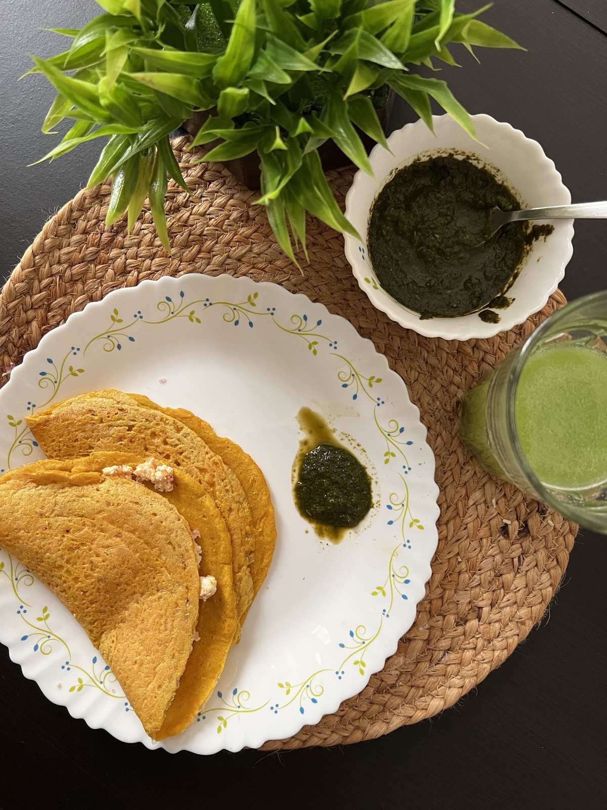Golden moong dal chilla with mint chutney and a green smoothie on a wicker mat
